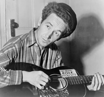 Woody Guthrie with guitar labeled 'This Machine Kills Fascists.'